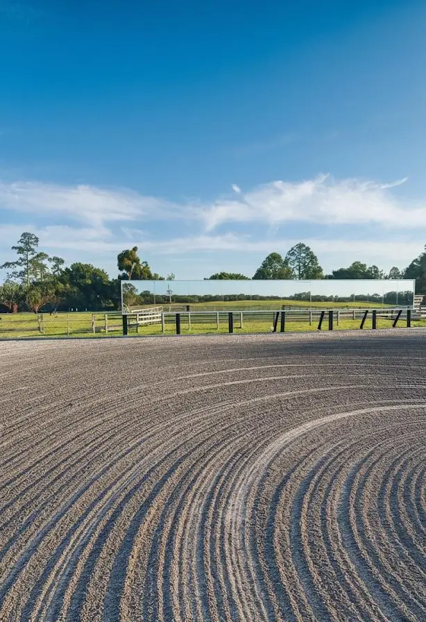 Freshly groomed arena footing curving toward the mirrored fence line